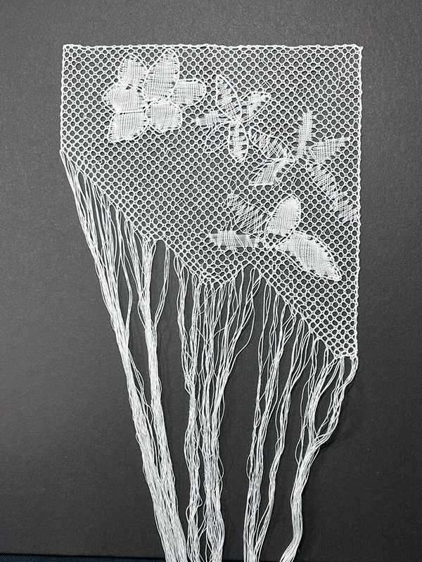 Completed Reality Torchon bobbin lace with jagged unfinished edge and hanging threads.