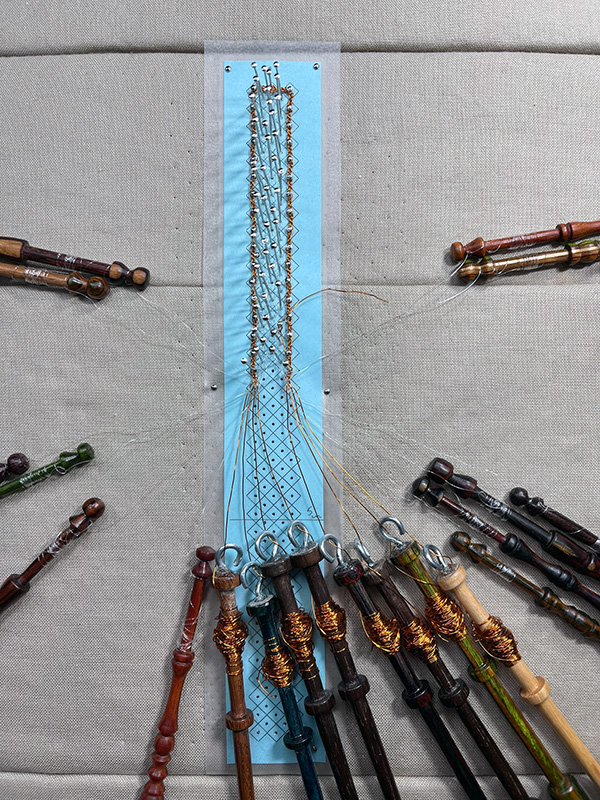 Narrow strip of bobbin lace made with fishing line and copper wire.