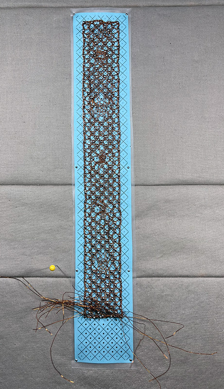 Wire lace still on the bobbin lace pillow.