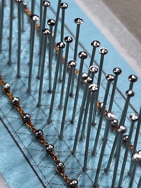 Close up picture of a narrow strip of bobbin lace made with fishing line and copper wire.