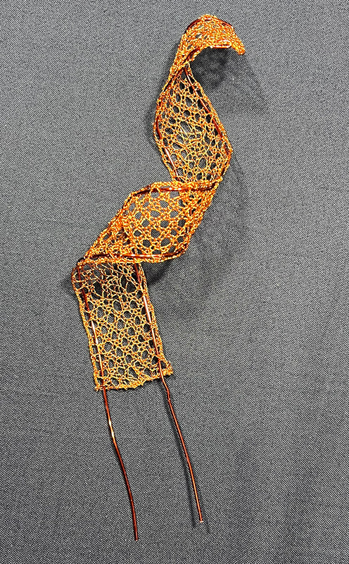 Curved bobbin lace strip with support wires.